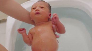 Asyalı yenidoğan bebeğin küvette banyo yapması. Anne oğlunu ılık suda yıkıyor. 7 gün boyunca yeni doğan bebek gülüşü küvette rahatlıyor ve rahatlıyor.
