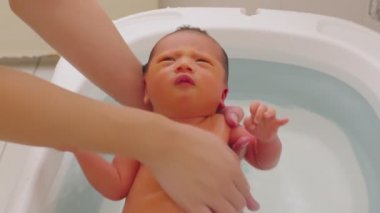 Asyalı yenidoğan bebeğin küvette banyo yapması. Anne oğlunu ılık suda yıkıyor. 7 gün boyunca yeni doğan bebek gülüşü küvette rahatlıyor ve rahatlıyor.