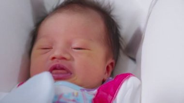 Bebek yatağında yatıp kameraya gülümseyen mutlu bir bebek masum gözleri rahat ve rahat bir Asyalı bebek. Yeni doğan bebek fotoğrafçılığı konsepti.