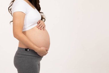 Yan manzara. Hamile kadın, beyaz arka planda izole edilmiş aşkla koca göbeğini okşuyor. Genç kadının hamileliği, gelecekteki hayattan, annelikten ve gebelikten zevk alıyor.