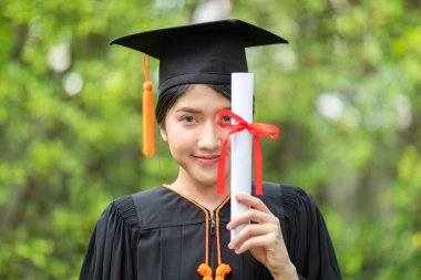 Çekici Asyalı Kadın Öğrenci Başlık ve cübbe ile mezuniyet töreni elinde sertifikayla ve gurur verici bir mutlulukla Mezuniyet Günü 'nde öğrenciyi ve Eğitim Başarı' nı kutluyor.
