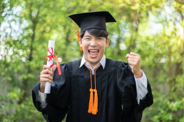 Asyalı Mezun adam elinde sertifikayla elini kaldırdı ve mezuniyet gününde çok gururlu ve mutlu bir şekilde kutladı. Mezuniyet gününde öğrencileri tebrik etti.