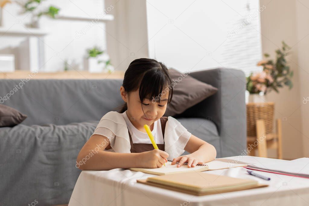 Portrait of little Asian girl child study learn at home smile and happiness.Cute girl drawing and handwriting in notebook to develop her skill and Emotional Quotient.Home School Education Concept