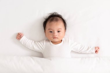 Üst görünüm mutlu bebek beyaz bir yatak ve battaniye uzanıyor rahat ve güvenli. Tatlı Asyalı yeni doğan bebek yatağa bakıyor. Yeni doğan bebek bakımı kavramı.