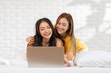 Güzel Asyalı genç lezbiyen çift ya da bilgisayar kullananlar birlikte gülümseyin ve yatakta rahatlayın. Mutluluk LGBTQ çifti evde birlikte vakit geçiriyor. LGBTQ Yaşam Biçimi Kavramı