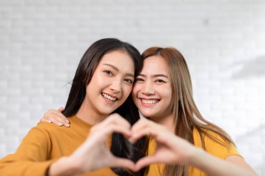 LGBTQ Asyalı lezbiyen çift kalp şeklinde birbirlerine sarılıyor ve sevgiyle gülümsüyor. Homoseksüel çift kucaklaşıyor ve kameraya bakıyor. Sevimli kız gülümsüyor ve bakıyor. LGBTQ Yaşam Tarzı Gurur Ayı