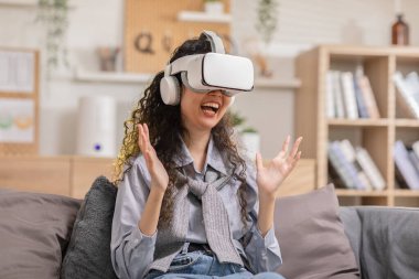 Sanal gerçeklik gözlüğü kullanan Asyalı kadın metaevrendeki nesneleri işaret ediyor. VR kullanan genç kadın gözlüğü evde eğleniyor. Evde 360 derece izleyip eğleniyor. Sanal Gerçeklik Ölçeği