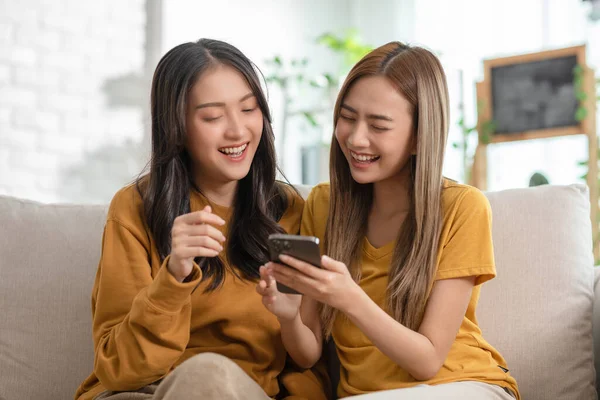 Lgbtqアジアのレズビアンの若いカップルは一緒に愛と携帯電話の幸福を使用して笑顔 スマートフォンを見て 自宅でソファで笑って陽気な同性愛者のカップルの友人 Lgbtqプライド月間 — ストック写真