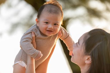 Mutlu Asyalı anne bebeği gün batımında birlikte oynayıp gülerek büyütür. Anne kızını sevgi ve güzel bir anla gökyüzüne kaldırır. Anne ve bebek konsepti.