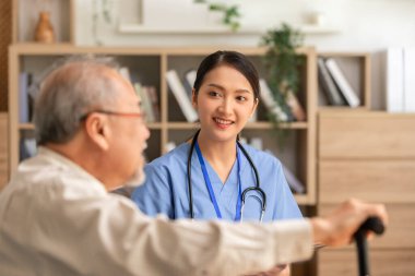 Asyalı doktor kadın, yaşlı ya da yaşlı hastaya teşhis koymak ve evde sağlık kontrolü yapmak için ziyarette bulundu. Mutlu yaşlılar, doktor ya da hemşireyle koltukta keyifli vakit geçiriyor.