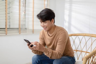 Asyalı adam iyi bir haber almış gibi cep telefonuyla gülümsüyor. Adam cep telefonu ekranından çok memnun görünüyor. Teknoloji bize kolaylık sağlıyor ve dünyayı küçültüyor..