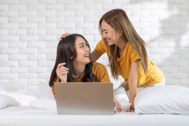 Güzel Asyalı genç lezbiyen çift ya da bilgisayar kullananlar birlikte gülümseyin ve yatakta rahatlayın. Mutluluk LGBTQ çifti evde birlikte vakit geçiriyor. LGBTQ Gurur Ayı Kavramı