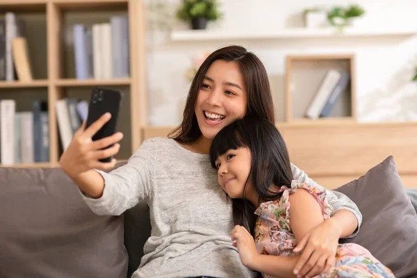 Asian mom and her kid are calling on smartphone. Both happy using cellphone for video call smiling mom and girl having fun greetings online with making video call communication through application.