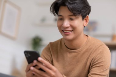Asyalı adam iyi bir haber almış gibi cep telefonuyla gülümsüyor. Adam cep telefonu ekranından çok memnun görünüyor. Teknoloji bize kolaylık sağlıyor ve dünyayı küçültüyor..