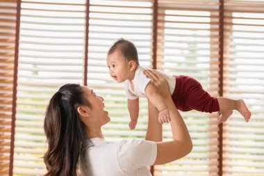 Yeni doğmuş bebek yatakta annesiyle oynarken mutlu ve mutlu. Anne evde gülümseyen ve neşeli. Bebek bebekle konuşurken gülüyor ve birlikte yeni doğmuş bebeği kusuyor.