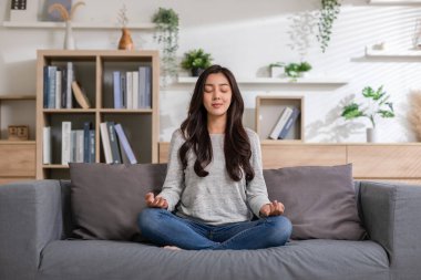 Yoga yapan Asyalı genç bir kadının istiridyesi meditasyon için poz veriyor ve evde çalışırken kanepede dinleniyor. İşten sonra çalışan mutlu bir kadın gözlerini kapatıp, yoga yaparak derin bir nefes alıyor..