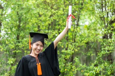 Çekici Asyalı Kadın Öğrenci Başlık ve cübbe ile mezuniyet töreni elinde sertifikayla ve gurur verici bir mutlulukla Mezuniyet Günü 'nde öğrenciyi ve Eğitim Başarı' nı kutluyor.