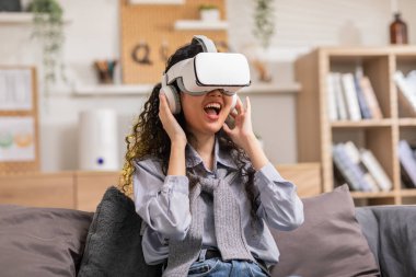 Sanal gerçeklik gözlüğü kullanan Asyalı kadın metaevrendeki nesneleri işaret ediyor. Gözlük kullanan genç bir kadın evde eğleniyor. Evde 360 derece izleyip eğleniyor. Sanal Gerçeklik Ölçeği