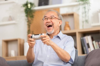 Heyecanlı, konsantre Asyalı yaşlı bir erkek televizyon ekranının önündeki koltukta oturmuş konsol ya da eğlence çubuğu kullanarak video oyunları oynuyor. Emekliliğin mutluluğu.