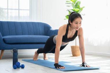 Antrenman yapan Asyalı bir kız evde paspaslar üzerinde egzersiz yapar omuz kası üzerinde yoğunlaşır. Oturma odasında kardiyo egzersizi yaparak antrenman yapan bir kadın. Elf konsepti.