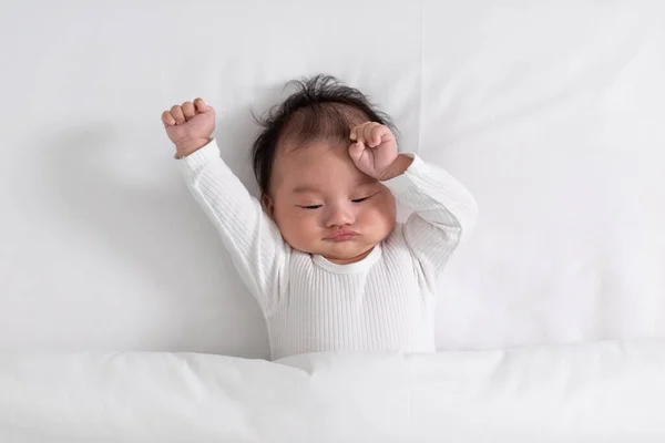 上から見る幸せな新生児の横になり 白いベッドと毛布の快適さと安全性にストレッチ かわいいアジアの幼児は目を閉じて寝るようになります 新生児ケアの概念 ロイヤリティフリーのストック写真
