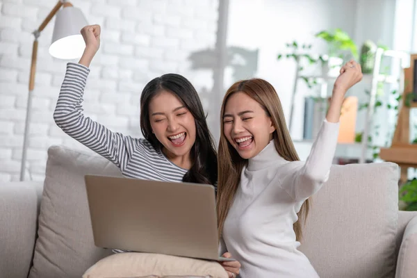 Mutlu genç Asyalı çift dizüstü bilgisayar kullanarak kanepede oturup video izliyor. Her ikisi de ekrana bakıp gülerek cihaza iyi haberi veriyor. LGBT konsepti ve LGBT topluluğu.