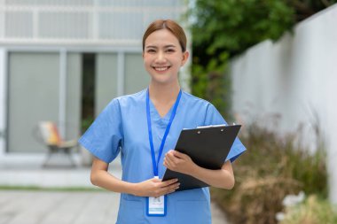 Steteskop gülüşlü Asyalı kadın doktor kameraya bakıyor. Hemşireler, iç açıcı bir gülümseme takınıyorlar. Olumlu duygusal ve iyi bir an.
