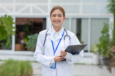Kameraya bakan steteskop gülüşlü Asyalı kadın doktor. Doktor kadın, beyaz önlüklü bir gülümseme takınıyor. Rahatlatıcı bir gülümseme. Pozitif duygusal ve iyi bir an.