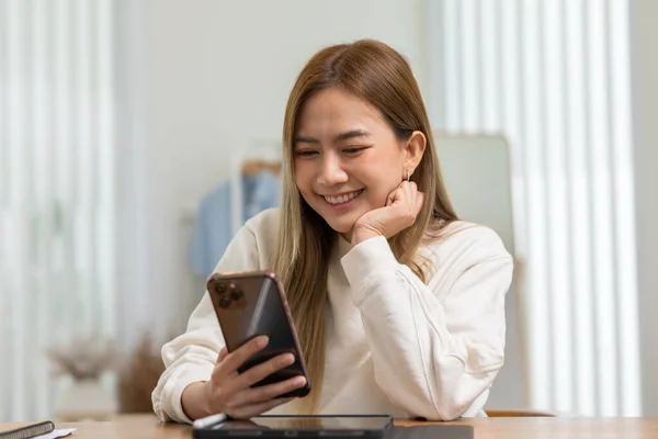 自宅でオンラインショッピングのための良いニュースや割引券で笑う携帯電話を探している千年紀のアジアの若い女性 — ストック写真