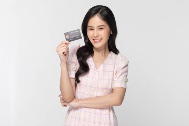 Kendine güvenen Asyalı genç kadın gülümsüyor ve kredi kartıyla mutlu oluyor. Neşeli bir kadın, sıradan bir şekilde kameraya bakıyor kredi kartının keyfini çıkarıyor ve beyaz arka planda sürpriz yapıyor. Kredi kartıyla mutlu.