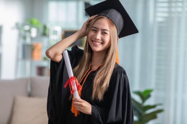 Şapka ve cübbe giymiş, gülümseyen, elinde sertifika ya da diplomayla gurur duyan, diplomasını başarıyla alan genç bir kadın, mezuniyet töreni konsepti.