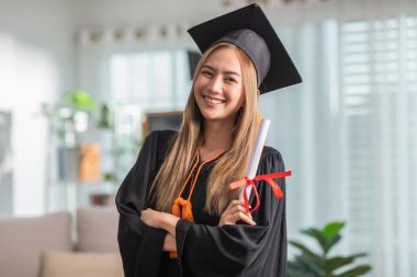Şapka ve cübbe giymiş, gülümseyen, elinde sertifika ya da diplomayla gurur duyan, diplomasını başarıyla alan genç bir kadın, mezuniyet töreni konsepti.