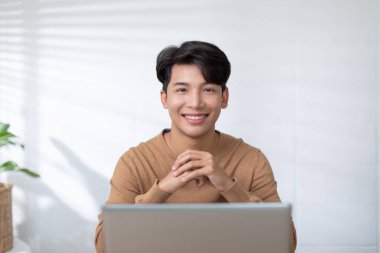 Girişimci yakışıklı iş adamı masa başında çalışırken gündelik tişört giyer gülümseme ve ev bilgisayarında mutlu olur. Ev işlerinde online satış pazarlama yapan serbest çalışan bir adam.