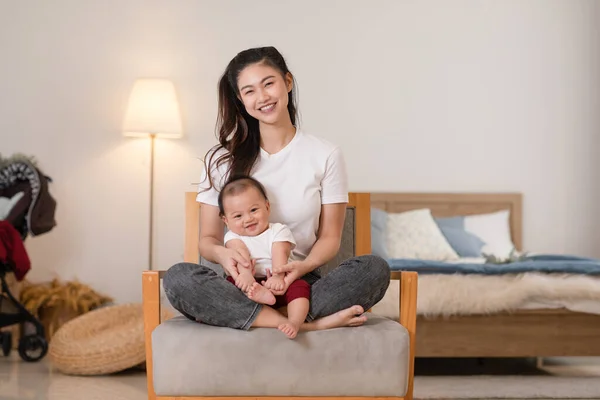 Happy asian mom playing and spending time with her newborn baby and looking at camera together at home.Adorable baby boy smile laughing with mother in warmth place relax and comfortable.good moment