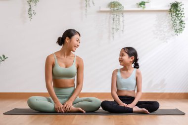 Mutlu Asyalı anne ve küçük kız yoga minderinde oturup birlikte gülüyor ve evde yoga yapmaya hazırlanıyorlar. Sağlıklı anne ve kız, yoga egzersizleri ve sıcak bir ortam. Güzel bir an.
