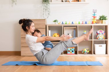 Asyalı anne yoga egzersiz dengesi yapıyor. Yoga minderinde sevimli bir bebek var. Gülümsüyor ve evde mutlu. Rahatlama zamanı. Bebek ve Anneler Günü