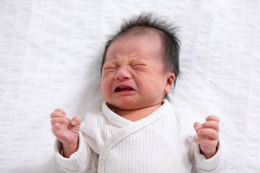 Crying and angry Newborn baby boy lying on white bed at home.Infant baby screaming very hungry or stomach pain. sick asian baby crying and having fever. Tired baby crying concept clipart