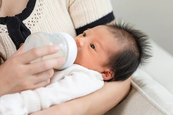 Close up hand of mother holding milk bottle Newborn baby lying on bed drinking milk at warmth place. Cute infant baby feeding milk good moment with love at home .Newborn Baby Concept