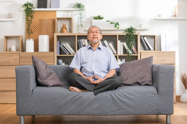 Mature Asian man doing yoga for meditation on yoga mat in living room at home.Clam of senior or elderly men meditation deep breath and relax at cozy home.Happy Retired Meditation at home concept