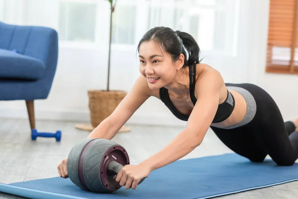 Athlete Asian young woman exercise with ab roller on exercise mat at home.Healthy female in sportswear workout exercise balance body on ab wheel roller to build strong muscle.Cardio Exercise Concept