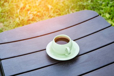 Sıcak bir yaz gününde, siyah ahşap bir masada bir fincan kahve. Masa yeşil çimlerin üzerinde, yakın plan.