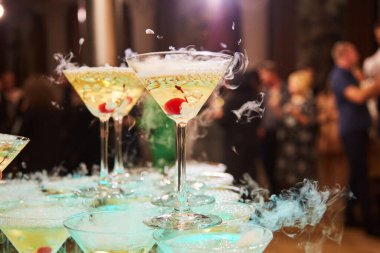 Cocktail glasses at an event or party. The glasses are on the buffet table. There is an alcoholic drink in the glasses, there is a cherry in the champagne glass
