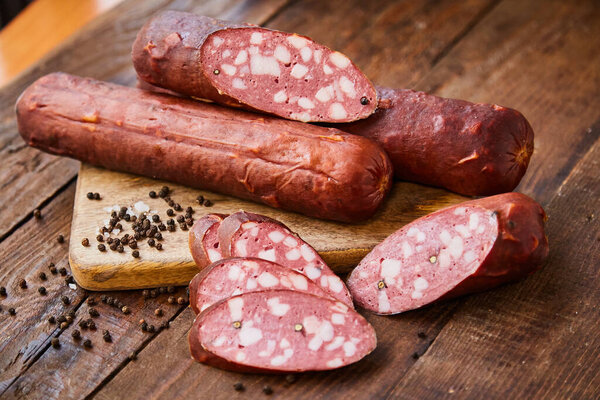 Homemade sausage with garlic cut into slices lies on a wooden table on a cutting board with spices and garlic. Traditional sausage, ready to eat, delicious breakfast. The concept of handmade meat products.