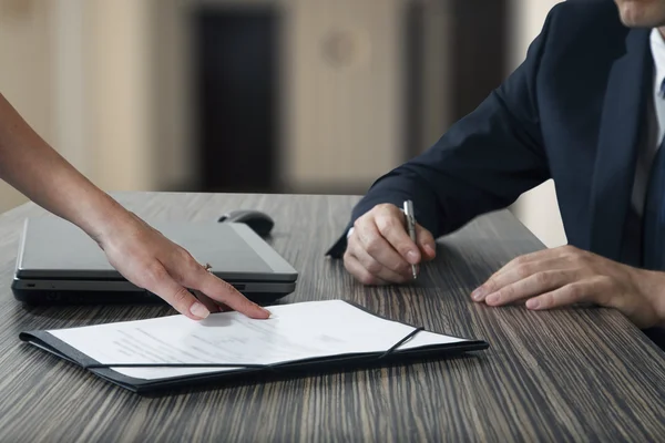 Vrouwelijke hand wijzend naar zakenman op handtekening plaats aan een contract document in office — Stockfoto