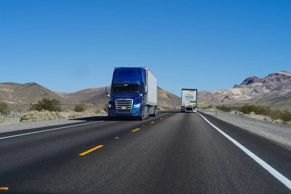Nevada, USA - February 26, 2022: image of semi trucks shown driving on a two lane highway near the town of Beatty in the state of Nevada.
