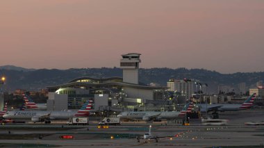 Los Angeles Uluslararası Havalimanı, Kaliforniya, ABD - 14 Ocak 2021: Bu görüntü önlük üzerinde birkaç Amerikan Hava Yolları jeti ve LAX 'te taksicilik yapan küçük bir sahne uçağı gösteriyor. Görüntü alacakaranlıkta alındı.