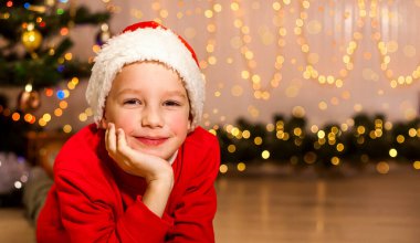 Noel Baba şapkalı küçük bir çocuk Noel ağacının yanında yatar ve kameraya bakar. Tatil kavramı - Noel, yeni yıl, Aziz Niklas Günü. Pankart. Metin için yer.