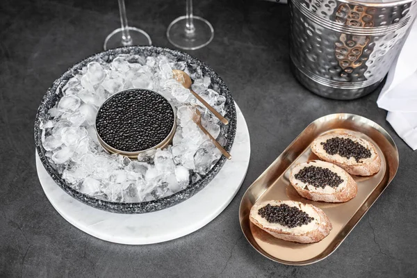 Zwarte kaviaar in blik op ijs, kaviaar sandwich op gouden bord, champagne in glas Stockfoto