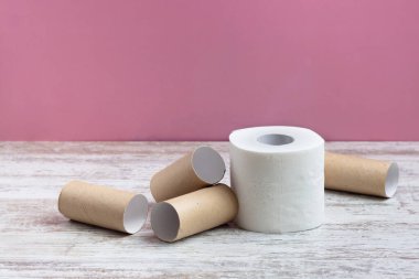 Boş tuvalet kağıdı rulolarının arasında bir rulo yumuşak beyaz tuvalet kağıdı. Pembe arka plandaki ahşap bir masada.