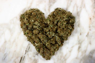 Kurumuş tıbbi marihuana tomurcukları mermer bir arka planda kalp şeklinde yatar.